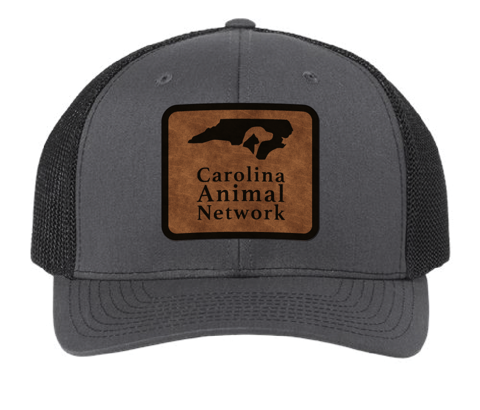Charcoal/black trucker hat featuring the Carolina Animal Network logo in a brown and black leatherette patch. Front view.