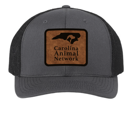 Charcoal/black trucker hat featuring the Carolina Animal Network logo in a brown and black leatherette patch. Front view.