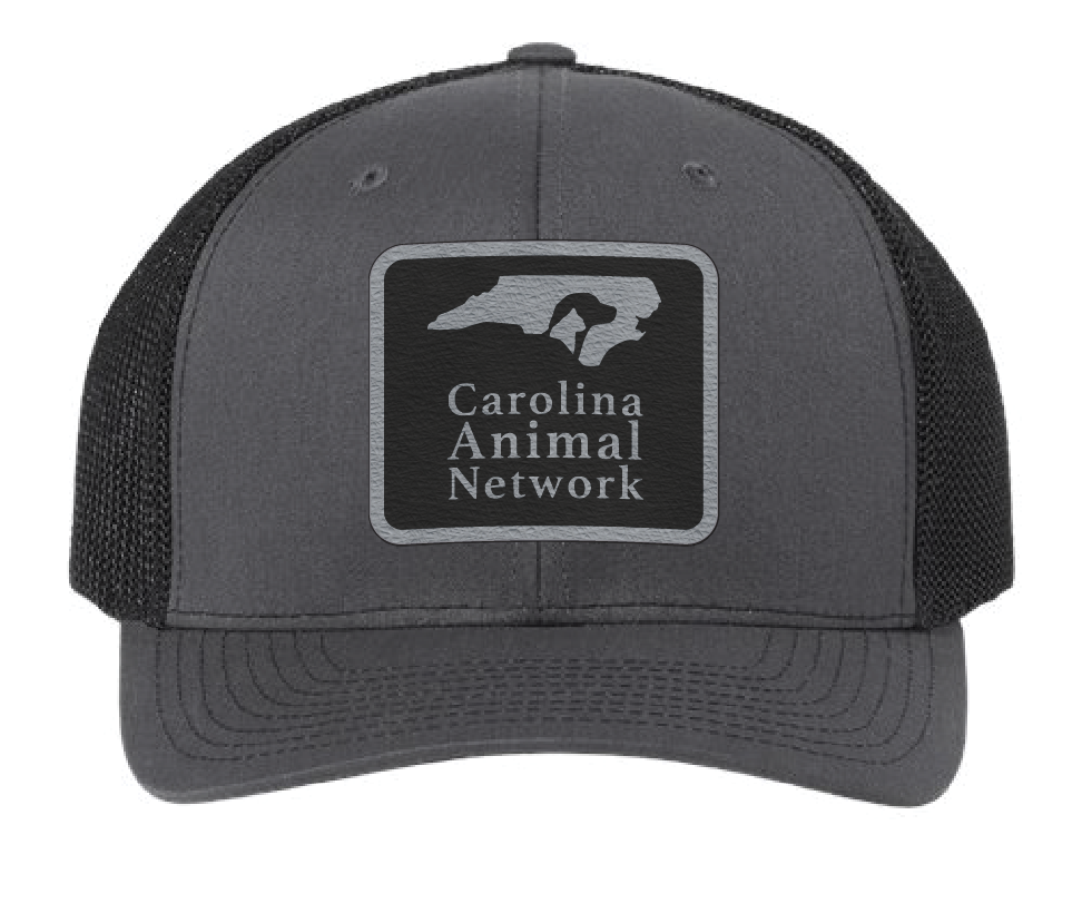 Charcoal/black trucker hat featuring the Carolina Animal Network logo in a black and silver leatherette patch. Front view.